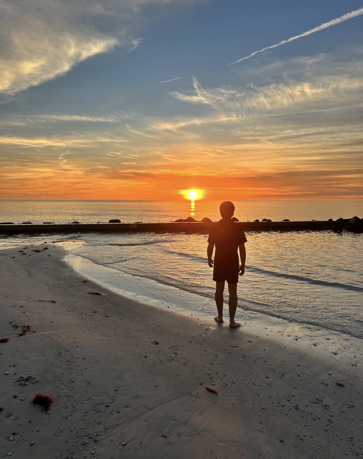 A person standing at the shoreline during an orange sunset