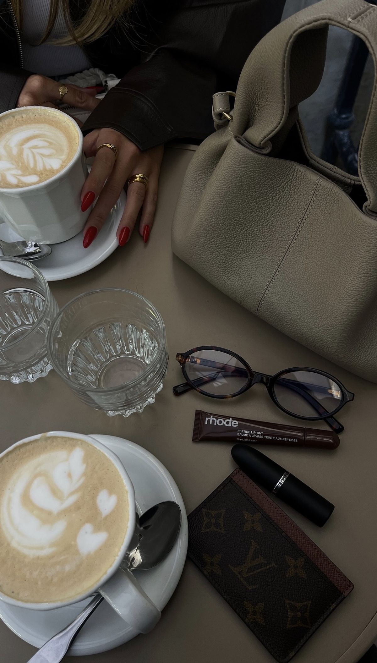 Cafe table with coffee, handbag, glasses, wallet, lipstick, and small essentials