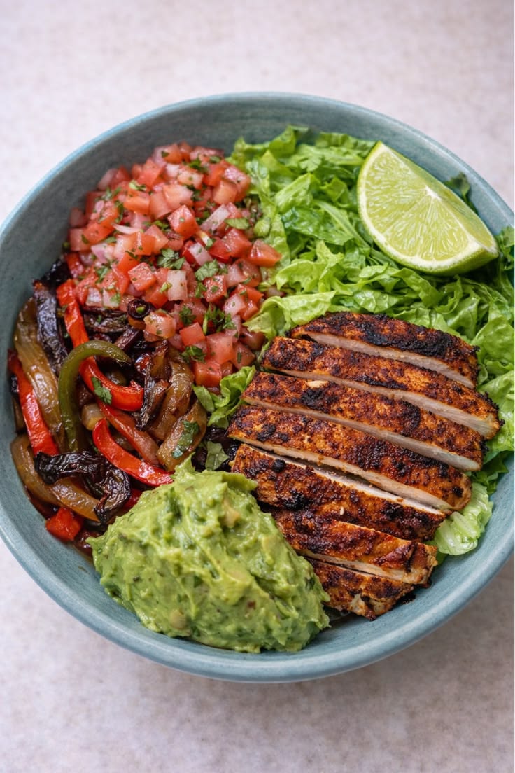 Chicken bowl with greens, peppers, tomato, avocado, and lime