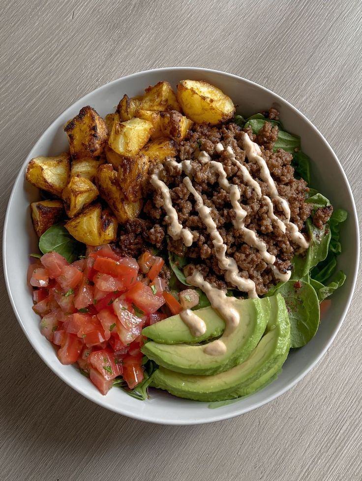 Balanced bowl with potatoes, ground beef, greens, tomato, and avocado