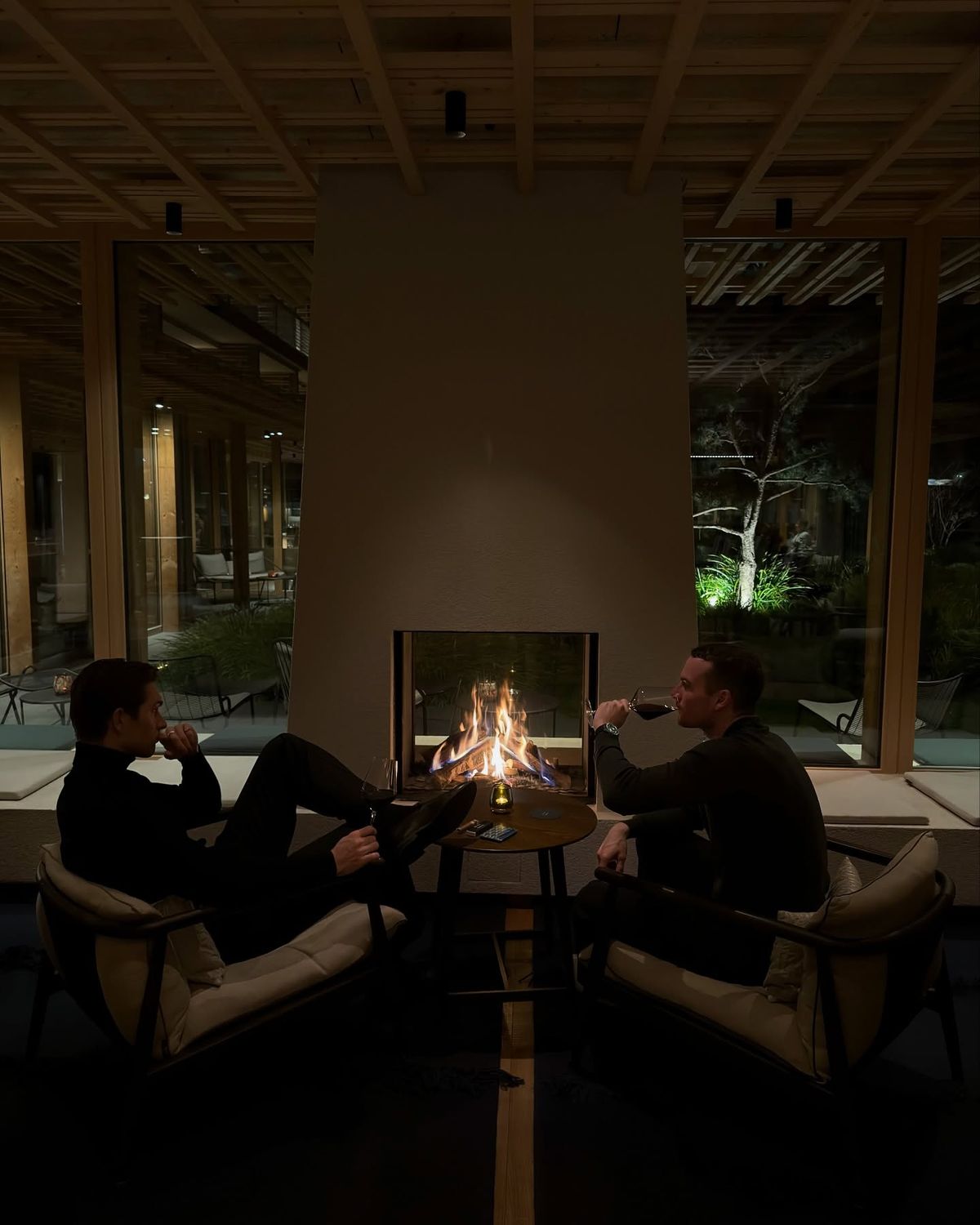 Two men sitting by a fireplace with wine in a warm interior