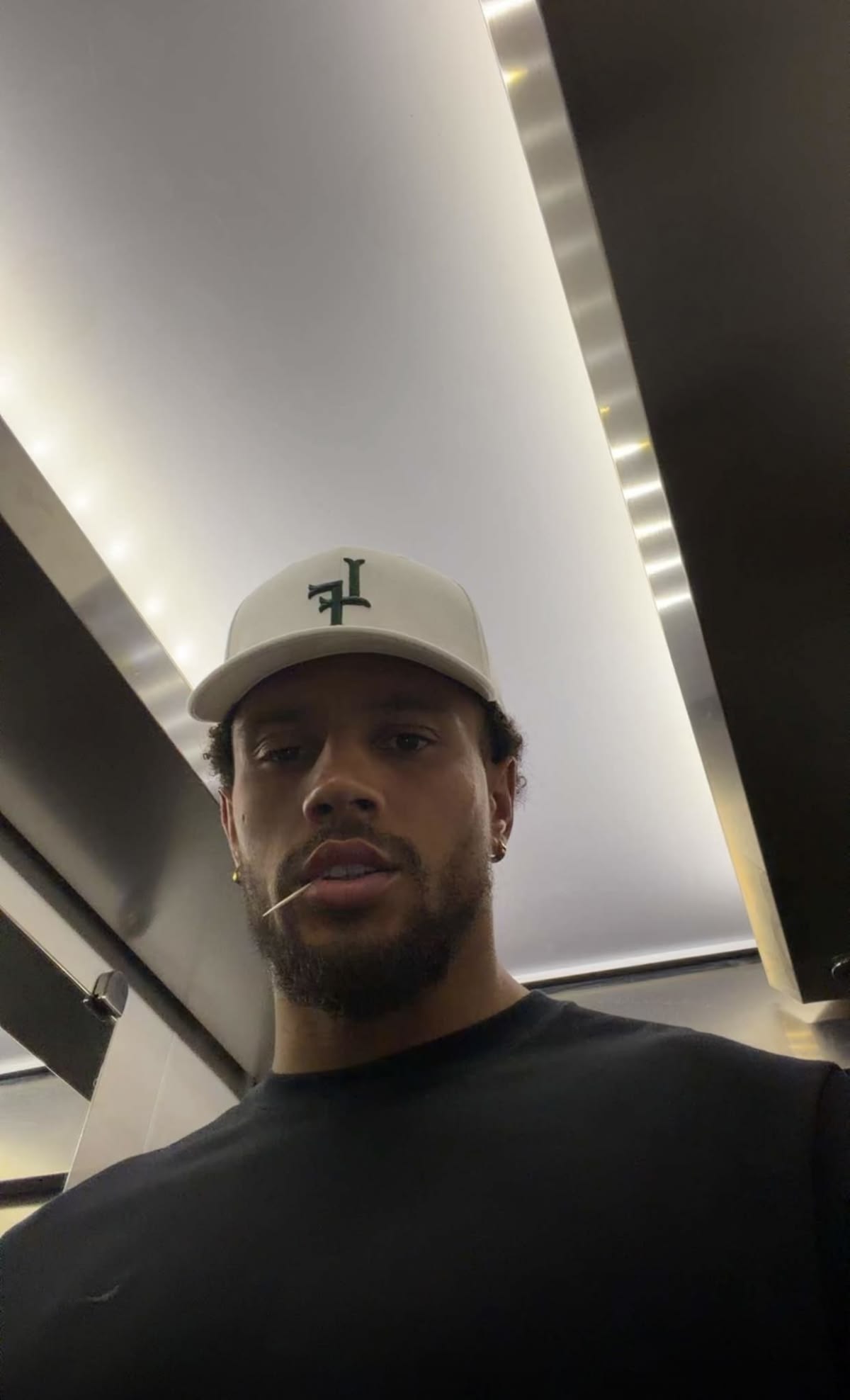 Man wearing a black tee and cream cap under soft light
