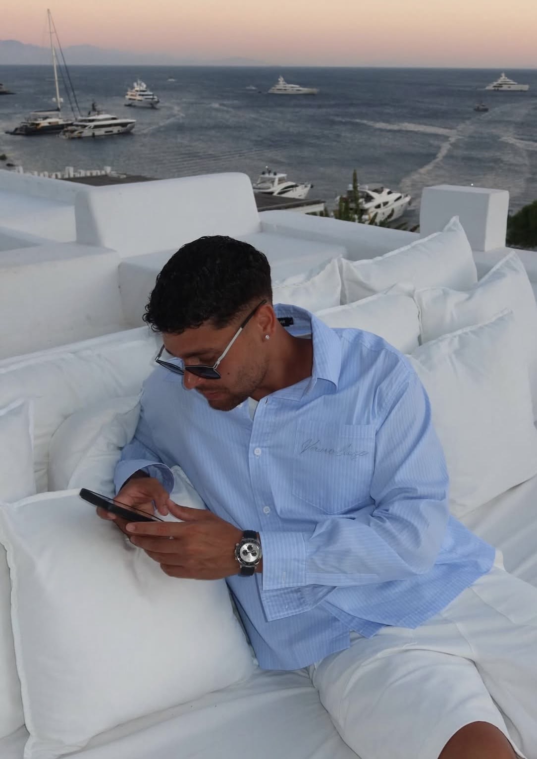 Man in a blue shirt and white shorts sitting outdoors by the water