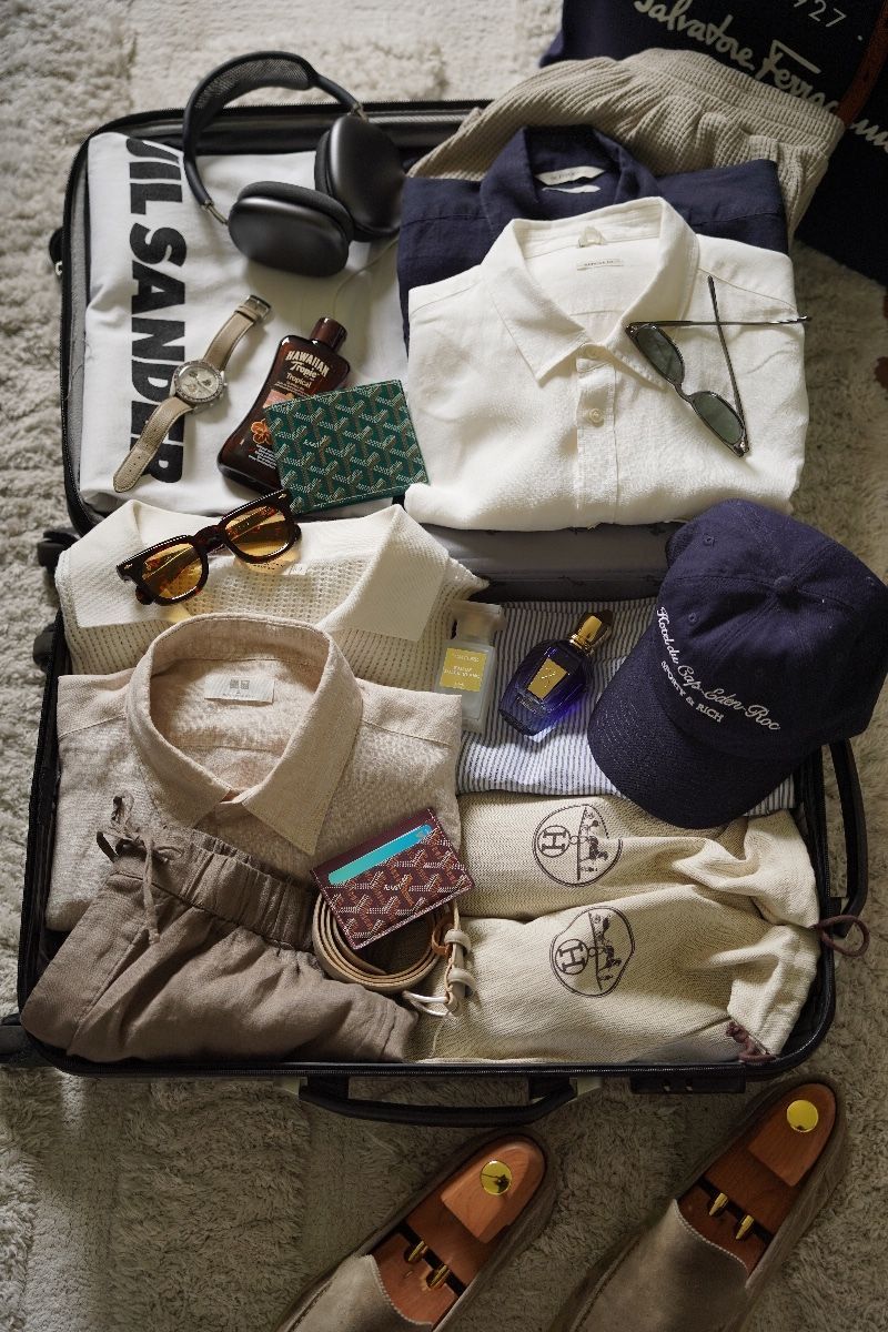 Open suitcase with folded clothes, watch, headphones, sunglasses, card holder, and loafers